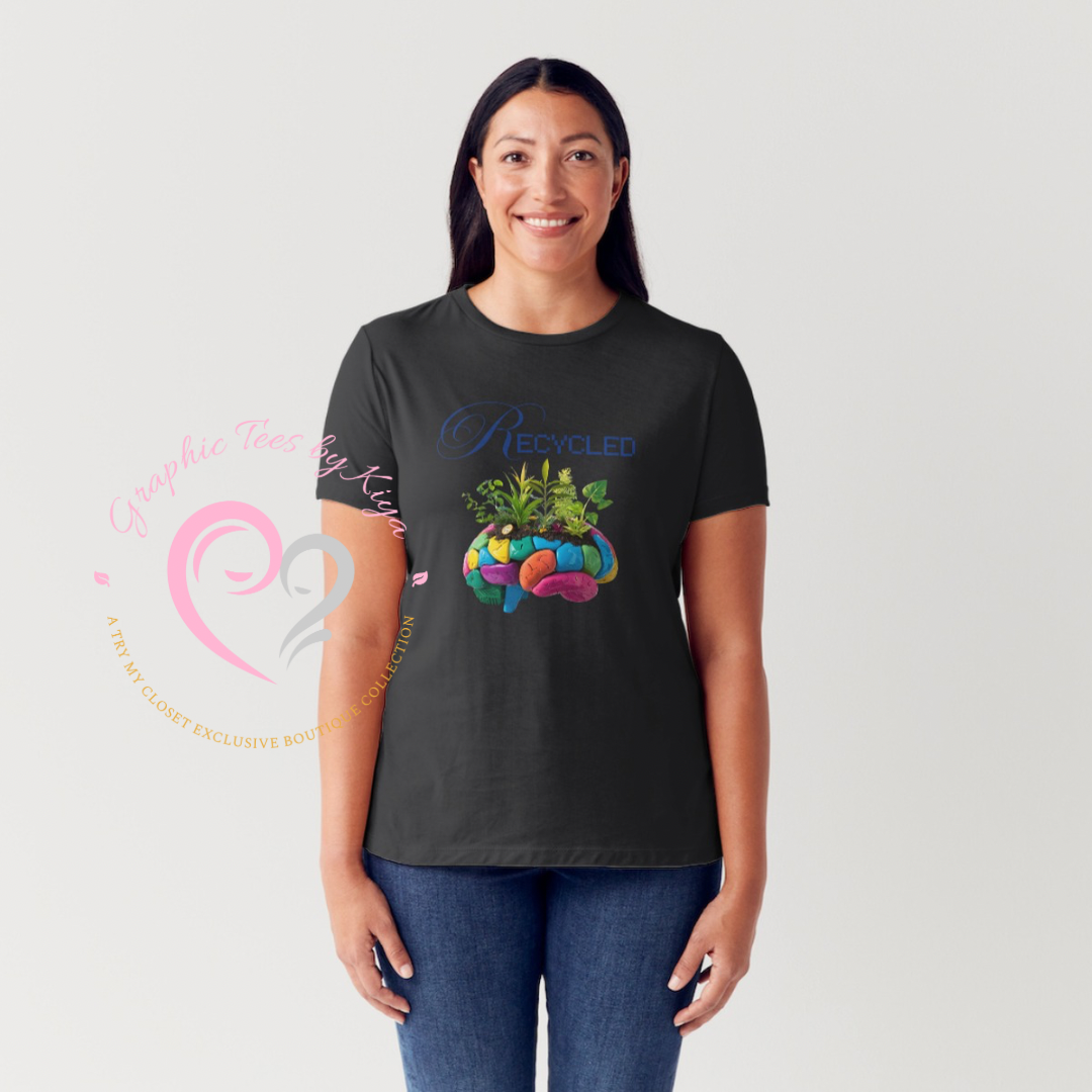 A smiling woman wears the Try My Closet Recycled Mind Graphic Tee—a black, eco-friendly shirt featuring a colorful brain labeled Recycled with sprouting plants. Shes against a plain background with a pink heart logo on the left.