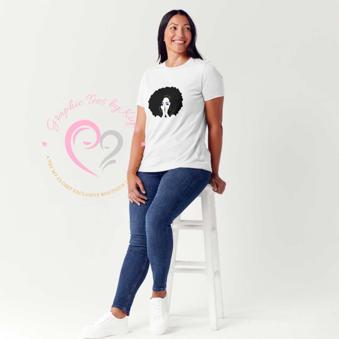A woman sits smiling on a white stool against a plain background, wearing blue jeans, white sneakers, and the Try My Closet Current Mood Graphic Tee featuring an afro design. The boutique logo appears overlaid on the image.