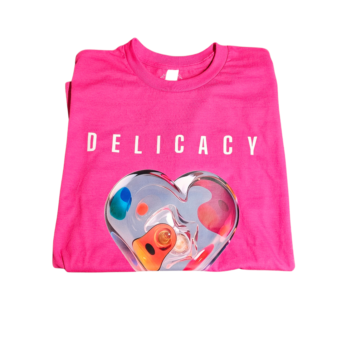 A folded bright pink Try My Closet Delicacy Heart Color Purple Changing Graphic Tee, featuring DELICACY in white and a colorful glass heart graphic, is displayed on a plain white background.