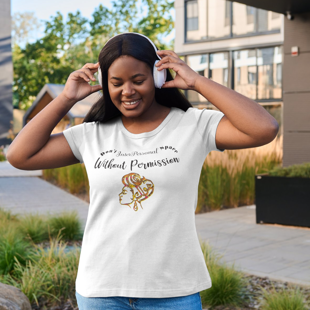 A smiling woman wearing headphones and the Inter Personal Space Graphic Tee by Try My Closet, featuring comic-style art and bold text, stands outdoors near modern buildings and greenery.