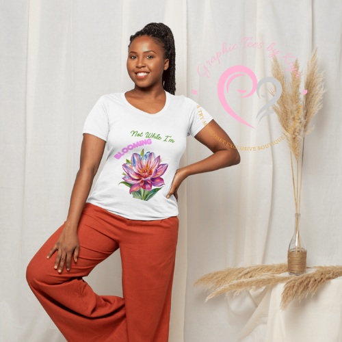A smiling woman indoors wears rust-colored pants and the Blooming Graphic Tee by Try My Closet, featuring a vibrant flower and Not While Im Blooming text. Dried pampas grass and a pink logo add charm. Custom orders available.
