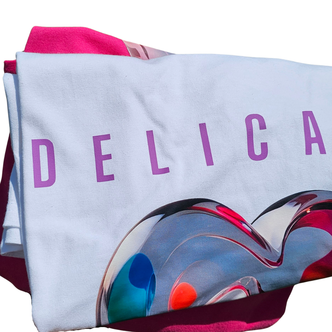 A folded Delicacy Heart Color Purple Changing Graphic Tee by Try My Closet features DELICA in purple and a glossy, colorful heart design, displayed on pink cloth. Ideal for custom orders and bold statements.