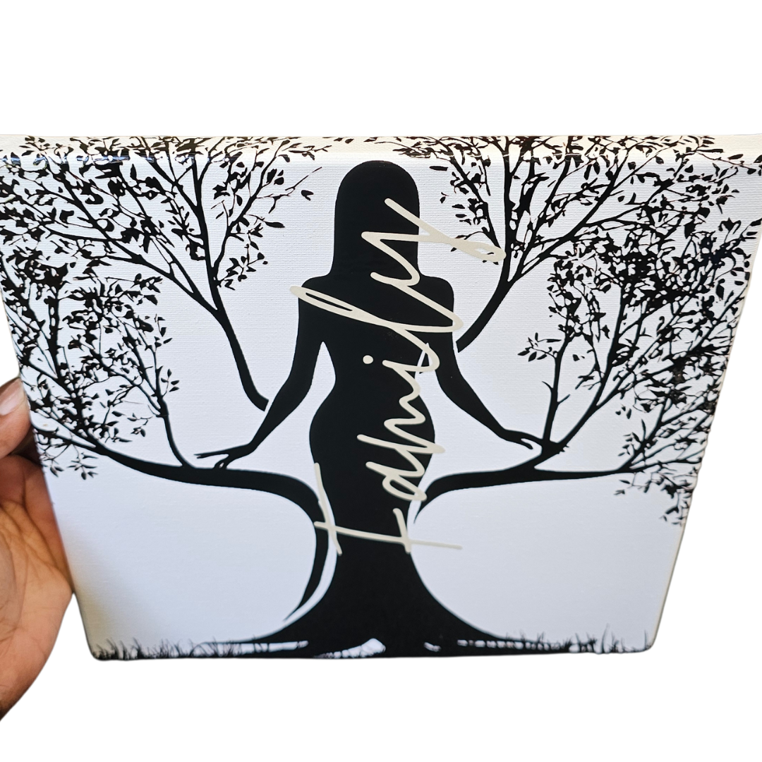A hand holds the Try My Closet Rooted Family Canvas 10x10, a white square wall art featuring a black silhouette of a woman whose flowing hair, arms, and dress blend into tree branches, with Feminism in gold script across the image.