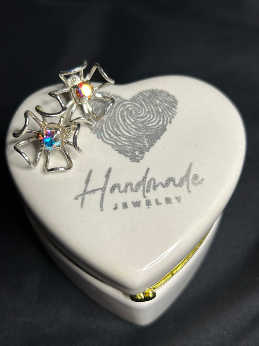 A heart-shaped ceramic jewelry box labeled Handmade Jewelry with a fingerprint design holds two Stunning Handcrafted Sterling Silver Flower Earrings w AB Prism Crystal by Delseys Treasures on its lid, set against a black background.