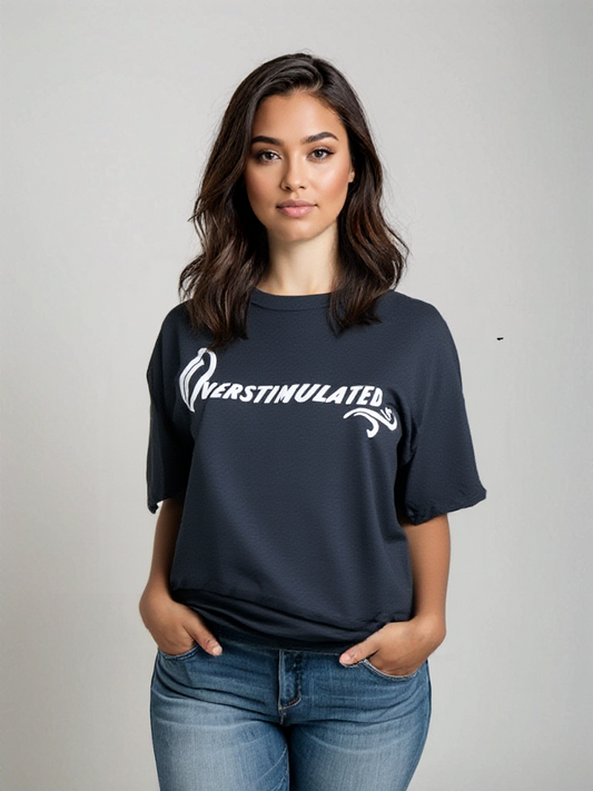 A woman with wavy brown hair wears the Try My Closet Overstimulated Black Graphic Tee, made from soft cotton, standing against a plain light background with her hands in her jeans pockets.
