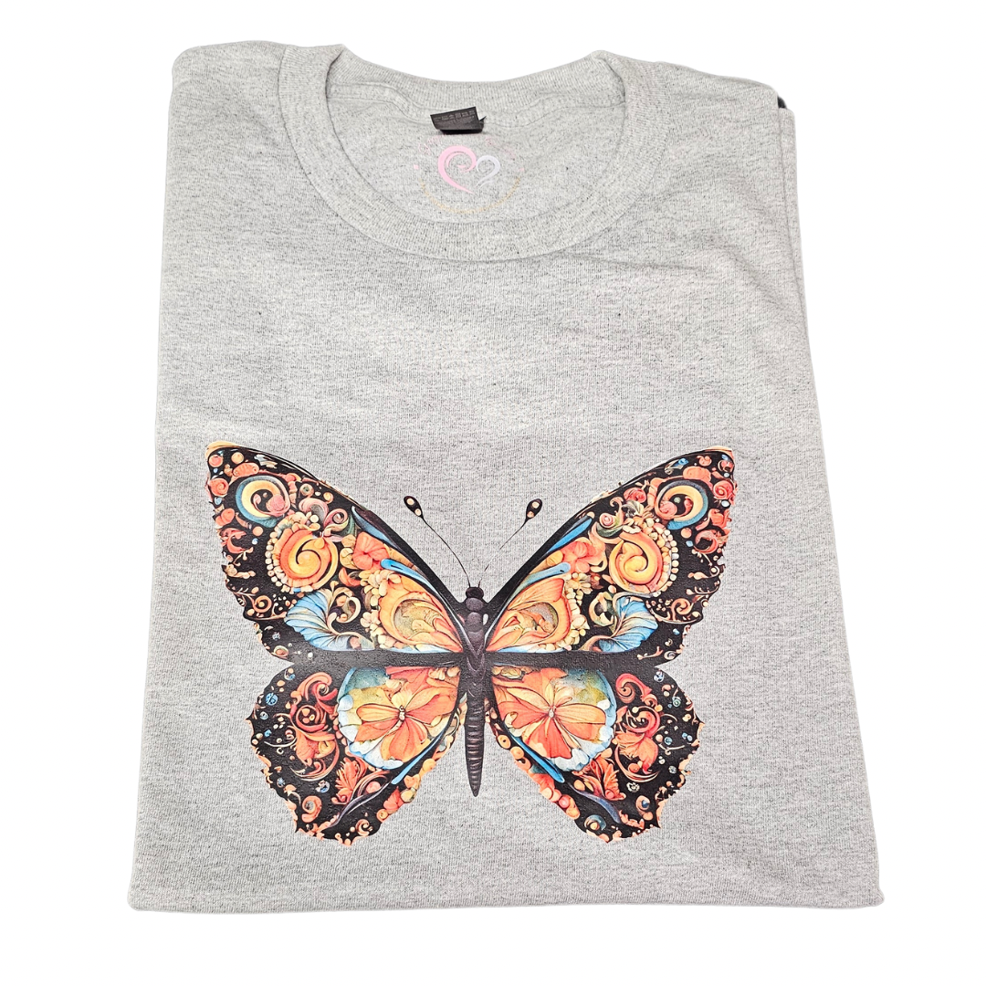 A folded light gray Morphed Graphic Tee by Try My Closet, featuring a vibrant butterfly graphic with ornate orange, yellow, blue, and black wing patterns on the front. Custom orders available.