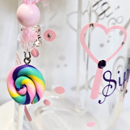 A close-up of the Try My Closet Sippie Sippie Lollipop Candy Color Changing Glass Tumbler, featuring pink hearts, dots, cursive text, and a handmade pastel beaded charm with a rainbow swirl lollipop.