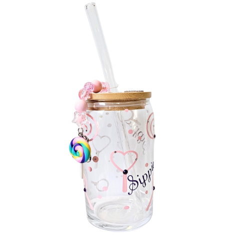 The Try My Closet Sippie Sippie Lollipop Candy Color Changing Glass Tumbler features pink heart and swirl designs, a glass straw, wooden lid, beaded lollipop pendant charm, and “Sippin” printed on the cup.